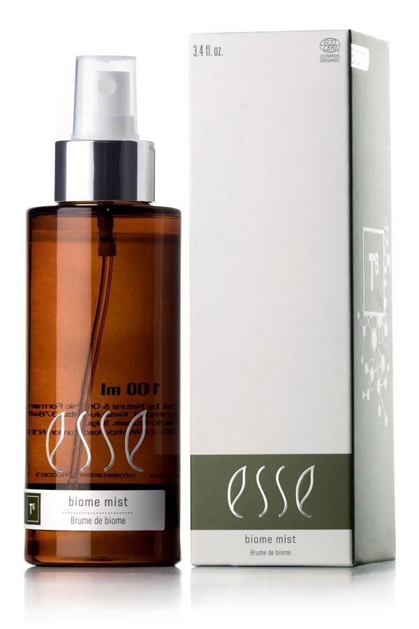 A bottle of Esse Biome Mist with a silver spray nozzle, housed in a brown container, is positioned beside its light green and white box package. Both the bottle label and the box prominently feature the brand name "Esse" along with the product description "Biome Mist." Additionally, the box is adorned with scientific graphics.