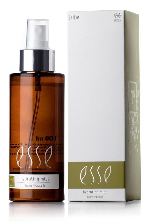 An Esse Hydrating Mist bottle in brown with a white pump is placed beside its matching white and green box. The bottle is labeled "100 ml" and "Hydrating Mist," while the box features consistent branding with "3.4 fl. oz." text.