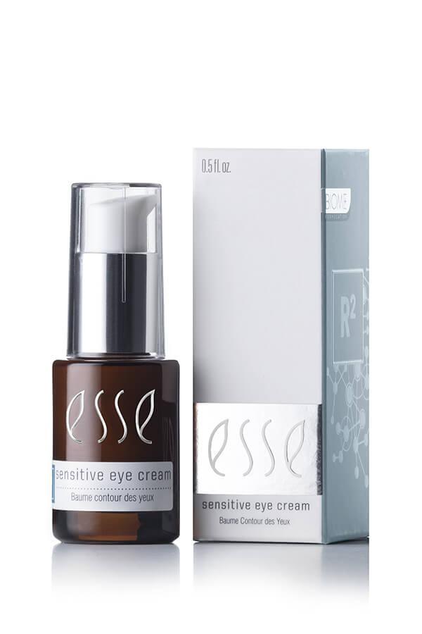 The image features a small bottle of Esse Sensitive Eye Cream beside its box packaging. The dark amber bottle, adorned with white text, includes a convenient pump dispenser. The light grey packaging displays matching white text and prominently shows the product name, Esse Sensitive Eye Cream.