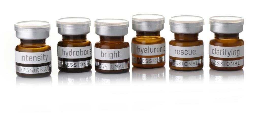 Six small amber glass bottles with silver caps are aligned. Each bottle is labeled with different text: "intensity," "hydroboost," "bright," "hyaluronic," "rescue," and "clarifying." The words "professional" are printed below each label.